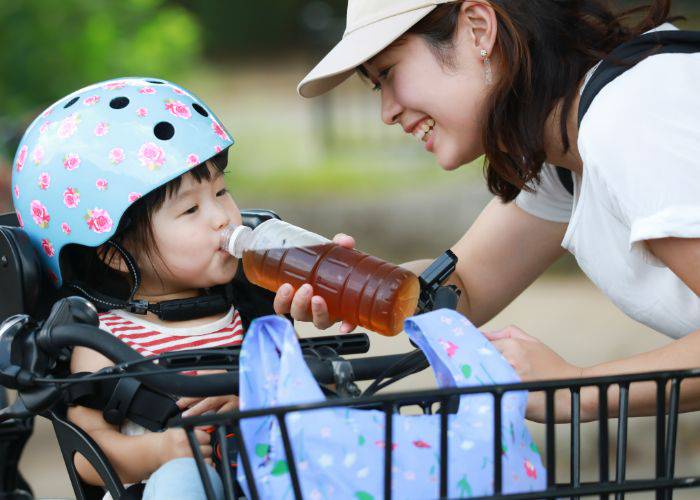 A child in the seat of a bicycle, sipping from a bottle of mugicha.